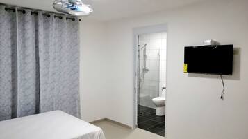 Una habitación de hotel con cama, televisor montado en la pared, zona de ducha y un inodoro.