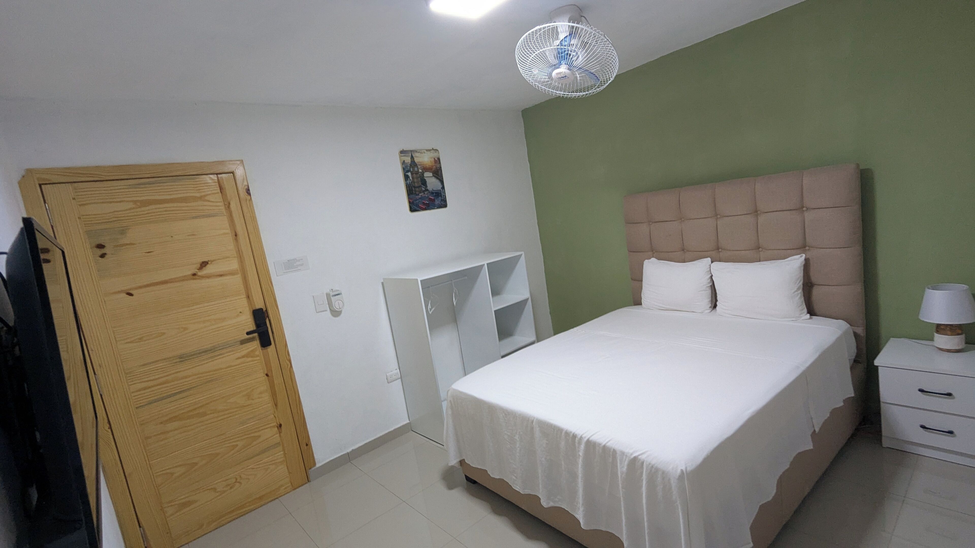A bedroom with a bed, a wardrobe, a bedside table, and a ceiling fan.