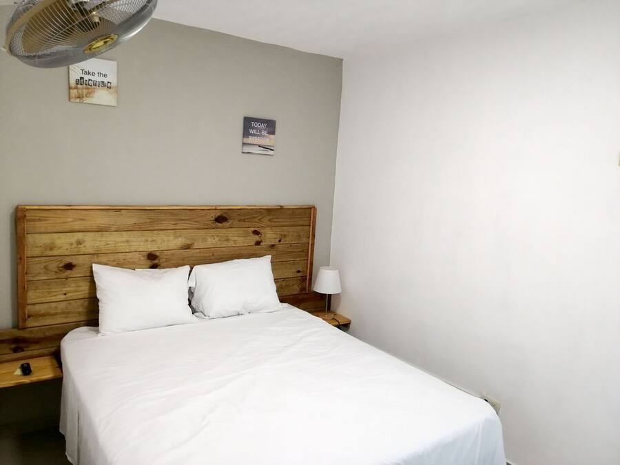 A bedroom with a wooden headboard, two white pillows, a white bedspread, a bedside lamp, and two wall-mounted signs.