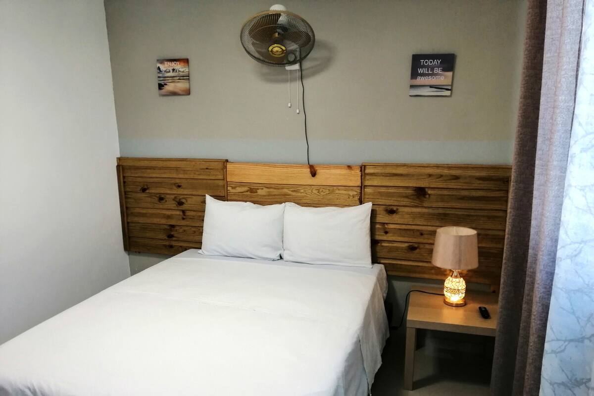 A neatly made bed with white linens, a wooden headboard, a bedside table with a lamp, and two motivational posters on the wall.