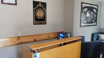 A hotel reception area with a wooden reception desk, a clock, a logo, a framed picture, and a blue sofa.