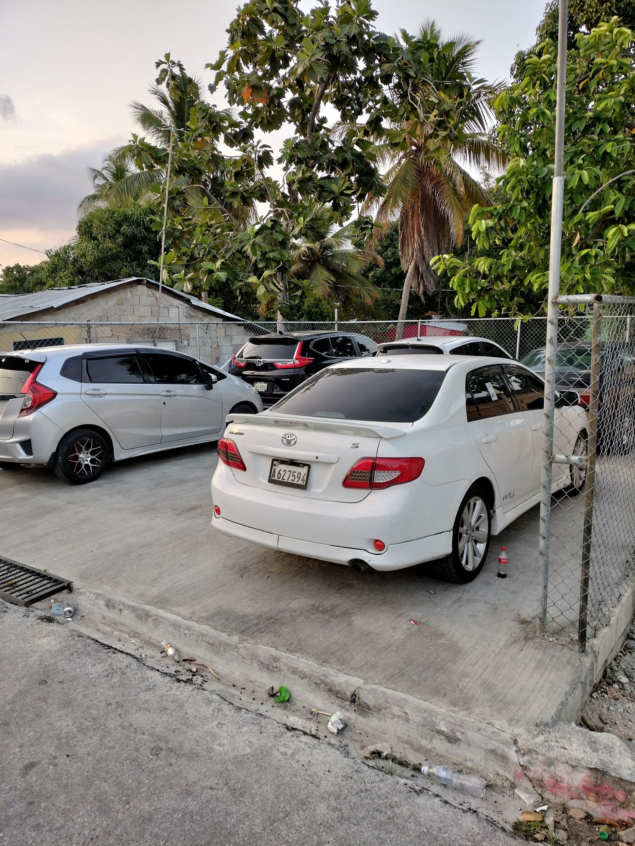 A parking area with several cars, including a white Toyota sedan, and a chain-link fence.