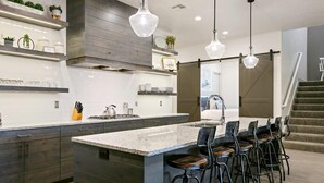 A modern kitchen with a large island, bar stools, and pendant lighting.