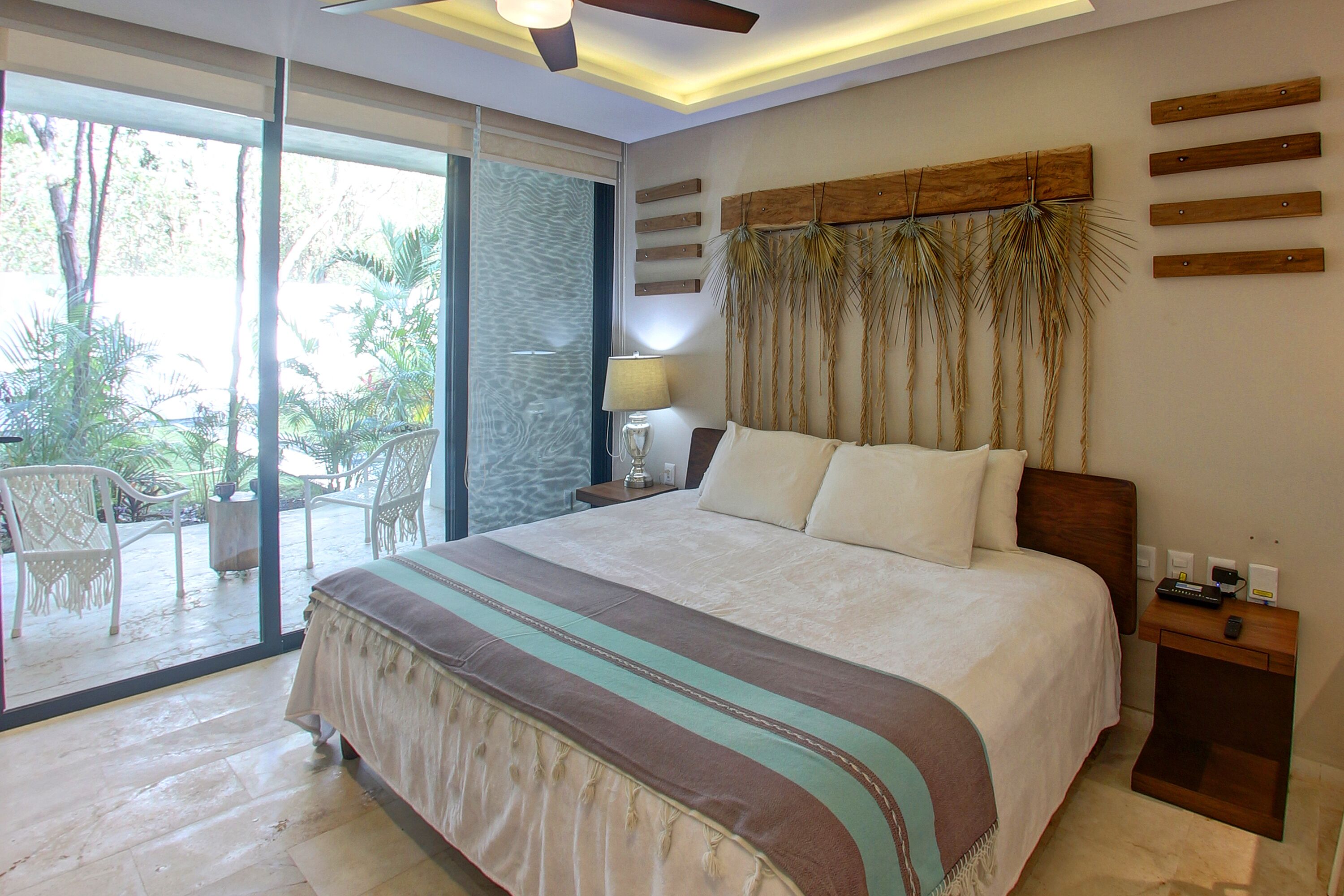 A spacious bedroom with a large bed, a ceiling fan, and a view of the outdoors through a sliding glass door.