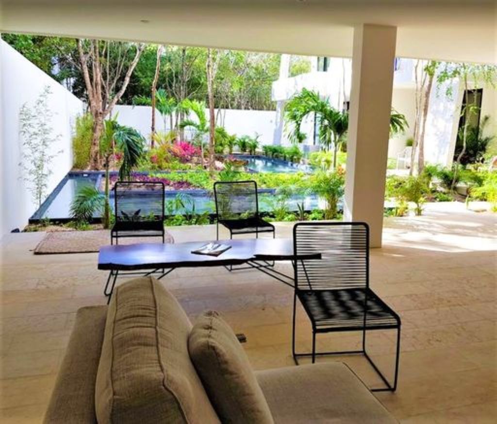 An outdoor patio with a table and chairs, surrounded by lush greenery and a swimming pool.