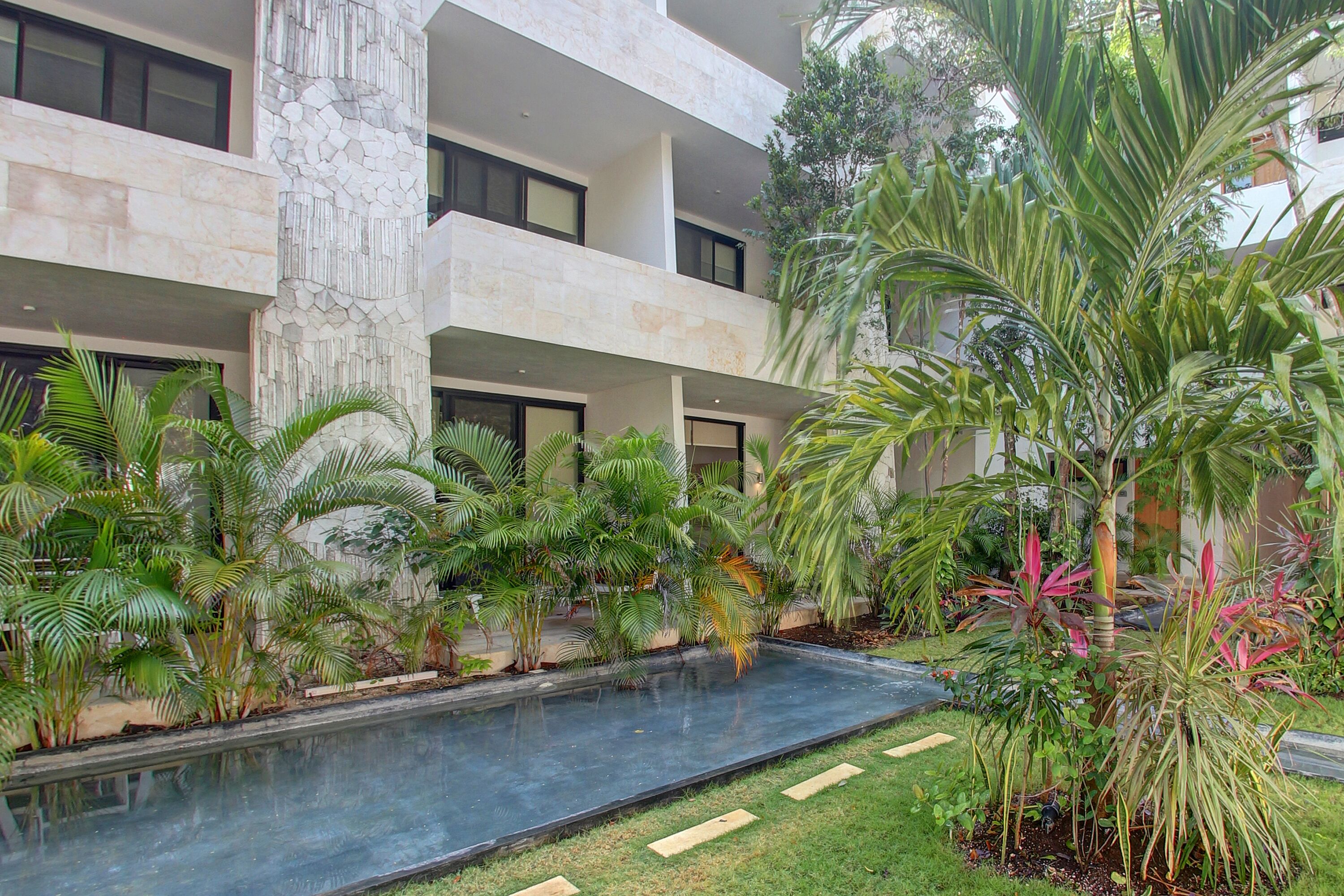A modern building with a pool, surrounded by lush greenery and palm trees.