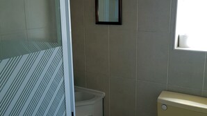 A bathroom with a toilet, a small trash bin, and a framed mirror on the wall. - Glen Villa Flat 3 - 4 Berth (Great Yarmouth)