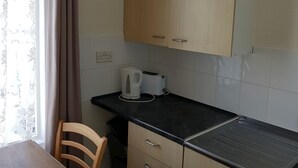 A kitchen with wooden cabinets, a black countertop, a kettle, and a toaster. - Glen Villa Flat 3 - 4 Berth (Great Yarmouth)