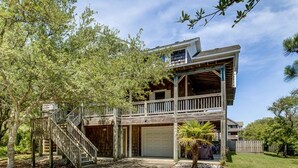 A two-story wooden house with a balcony, a garage, and a staircase leading to the upper level. - Seaside Memories | 930 ft from the beach | Private Pool, Hot Tub (Nags Head)
