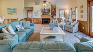 A spacious living room with a fireplace, a ceiling fan, and a bookshelf. - Seaside Memories | 930 ft from the beach | Private Pool, Hot Tub (Nags Head)