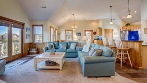 A spacious living room with a large sectional sofa, a coffee table, and a dining area with wooden chairs and a kitchen in the background. - Seaside Memories | 930 ft from the beach | Private Pool, Hot Tub (Nags Head)