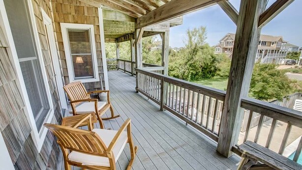 A wooden deck with two rocking chairs and a view of a residential area. - Seaside Memories | 930 ft from the beach | Private Pool, Hot Tub (Nags Head)