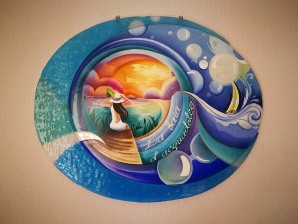 A circular wall art with a woman in a boat, a sunset, and the text "La baria l'acqua dolce".
