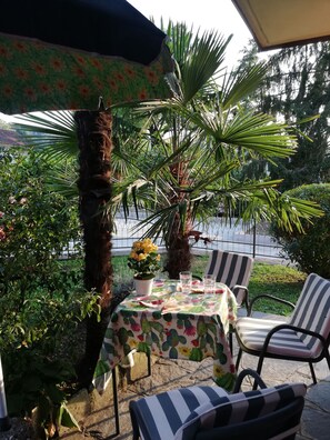 An outdoor patio with a table set for two, surrounded by chairs, a potted plant, and a cactus.