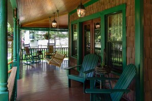 A covered porch with green Adirondack chairs, a rocking chair, and hanging lanterns.