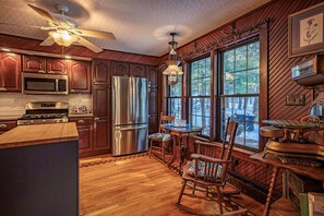 A kitchen with wooden cabinets, stainless steel appliances, a dining area with a table and chairs, and a large window with a view.