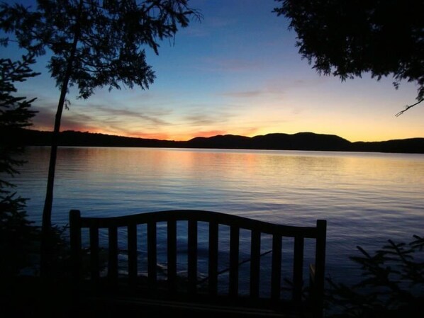 A bench overlooking a calm lake at sunset with distant hills.