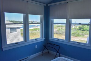 A room with large windows, a metal chair, and a view of a beach and buildings.