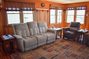 A living room with a beige recliner sofa, a leather armchair, a small table, and a patterned rug.
