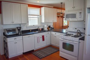 A kitchen with white cabinets, a stove, a microwave, and a coffee maker.