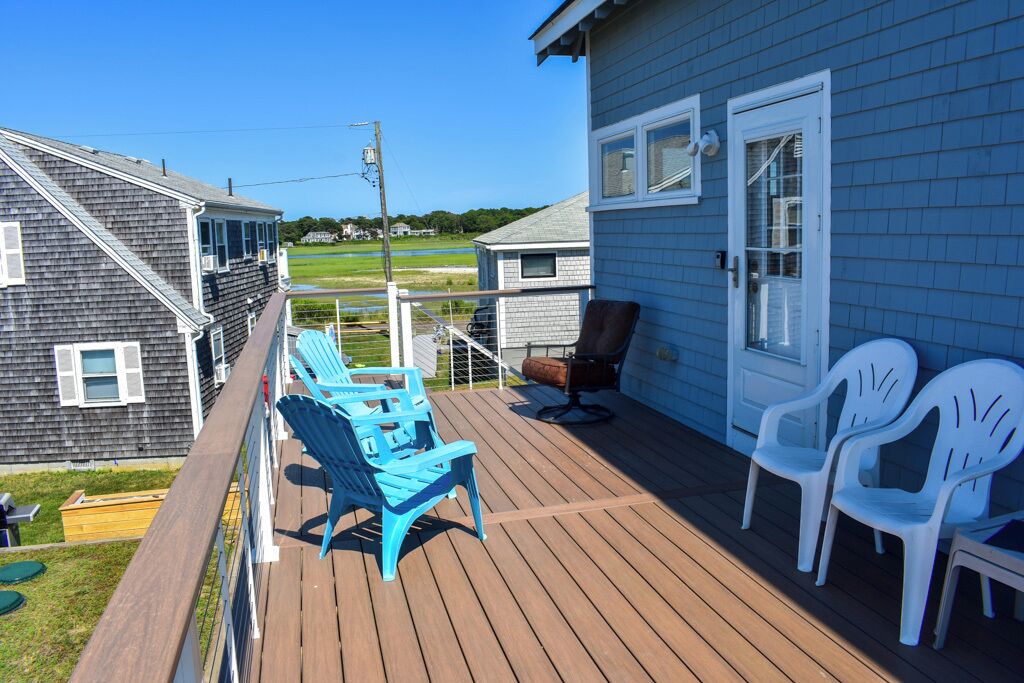 Une terrasse avec des chaises bleues et blanches, une chaise marron et une porte blanche.