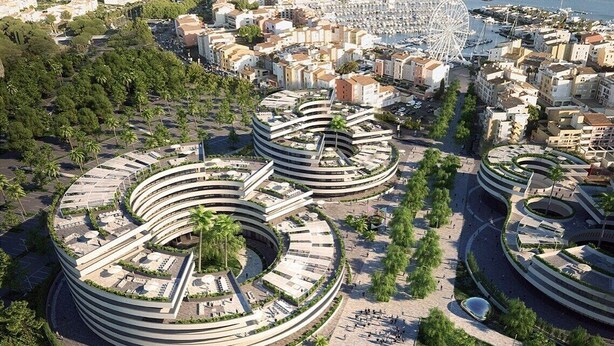 Et moderne arkitektonisk kompleks med runde bygninger, en lystbådehavn og et kystlandskab i baggrunden.