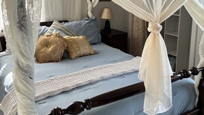 Una cama con dosel y cuatro postes, una mesita de noche con lámpara, y un cojín estampado.