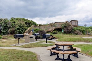 A picnic area with outdoor grills, picnic tables, and a wooden deck with stairs leading to a building.