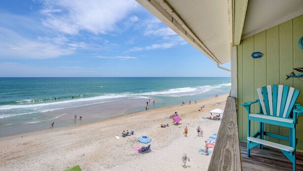 A beach view from a porch with a wooden deck, overlooking a sandy beach with people and umbrellas. - 2 Bedroom Direct Oceanfront (Surf City)