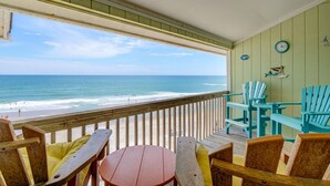 A wooden deck with a view of the ocean, featuring a wooden table and chairs, a clock, and wall decorations. - 2 Bedroom Direct Oceanfront (Surf City)