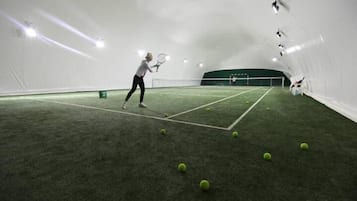 An indoor tennis court with a player practicing.