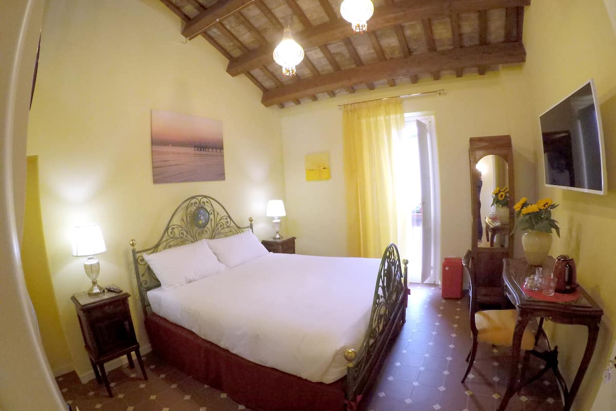 Een slaapkamer met een groot bed, een nachtkastje met lamp, een dressoir, een spiegel en een raam met gordijnen.