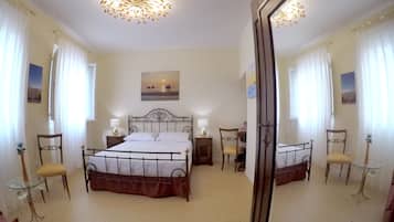 Un dormitorio con una cama, dos sillas, una mesa, un espejo y una lámpara en el techo.