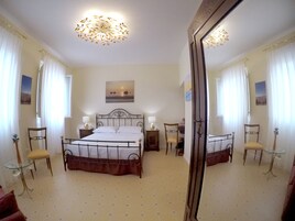 Un dormitorio con una cama, dos sillas, una mesa, un espejo y una lámpara en el techo.