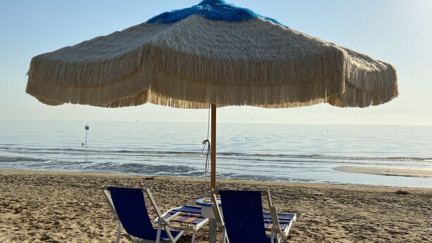 Una sombrilla de playa con dos sillas de playa debajo.