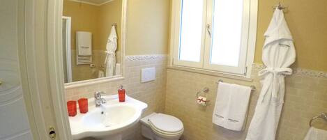 A bathroom with a sink, toilet, and a mirror. There are towels hanging on the wall and a robe on a hook.