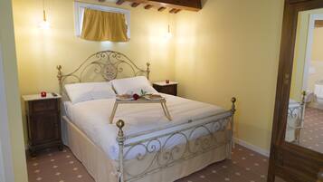A bedroom with a metal bed frame, a bedside table, a nightstand, a window with a curtain, and a mirror.