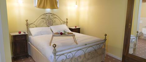 A bedroom with a metal bed frame, a bedside table, a nightstand, a window with a curtain, and a mirror.