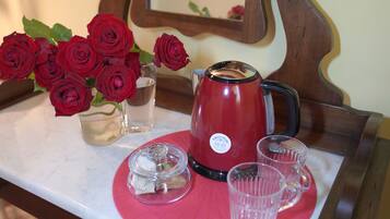 A table with a red teapot, two clear glasses, a glass jar with tea bags, and a vase with red roses.