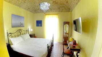A bedroom with a bed, a desk, a chair, a mirror, and a chandelier.