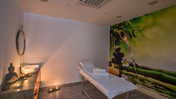 Experience serenity in this spa room with a minimalist design, featuring a massage table, Buddha statue, and tranquil mural.