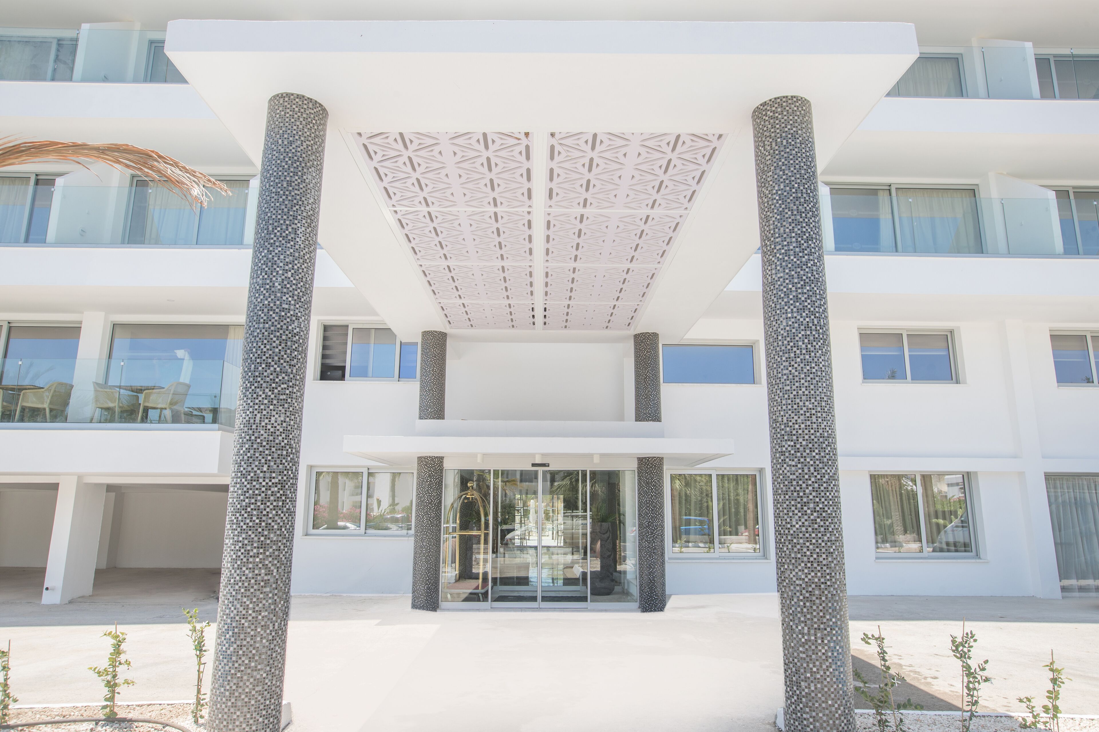 Un bâtiment moderne doté d’une entrée en verre, de façades blanches et d’un plafond au design géométrique.