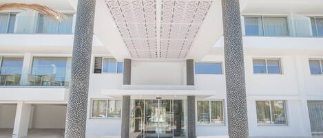 Un bâtiment moderne doté d’une entrée en verre, de façades blanches et d’un plafond au design géométrique.