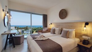 Habitación de hotel con una cama grande, un escritorio, una silla, una mesita y vistas al océano.