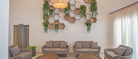A modern living room with a hexagonal wall design, grey sofas, round wooden coffee tables, and a hanging pendant light.