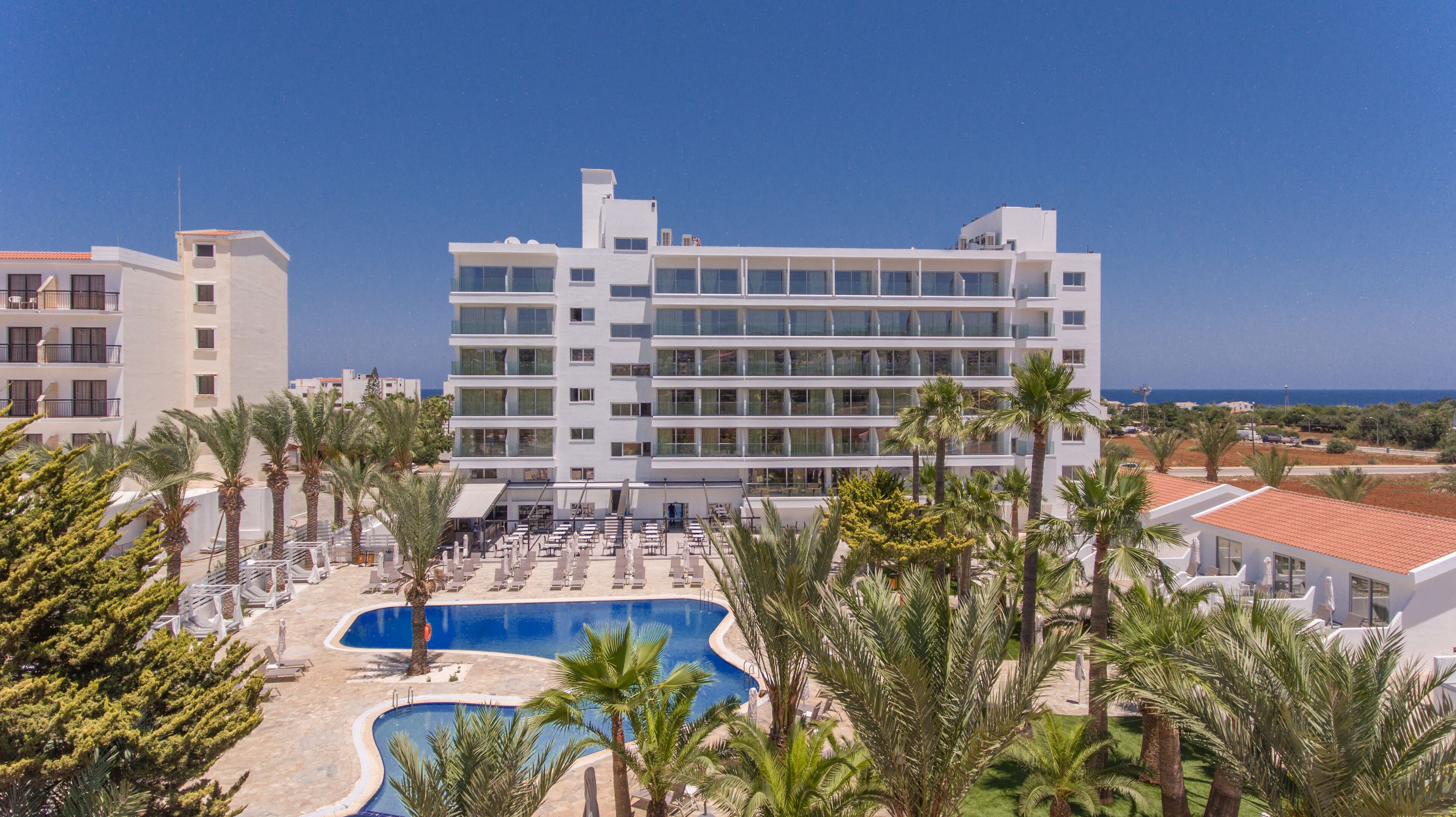 Un hotel moderno con piscina, palme e vista sul mare.