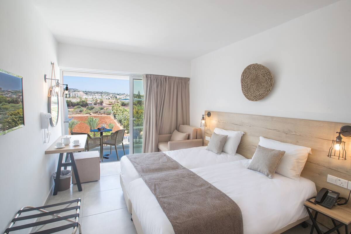A hotel room with a large bed, a desk with a chair, a small table, and a view of the city.