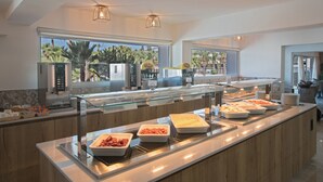 Un bufé con diversas opciones de comida y vistas a palmeras afuera.