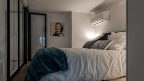 Un dormitorio moderno con cama, aire acondicionado de pared y un ventanal grande.