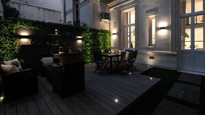 Un patio al aire libre con piso de madera, mobiliario y luces ambientales.